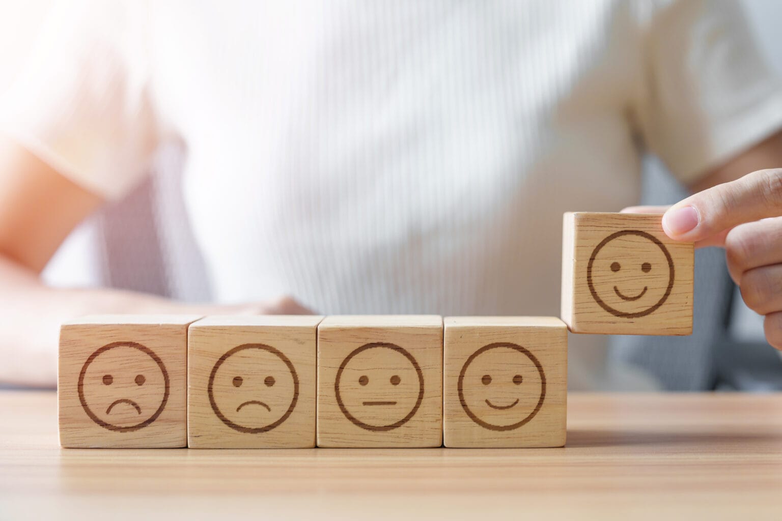 Employee Wellbeing positiv: Eine Hand wählt ein lächelndes Gesicht aus dem Emotionsblock.