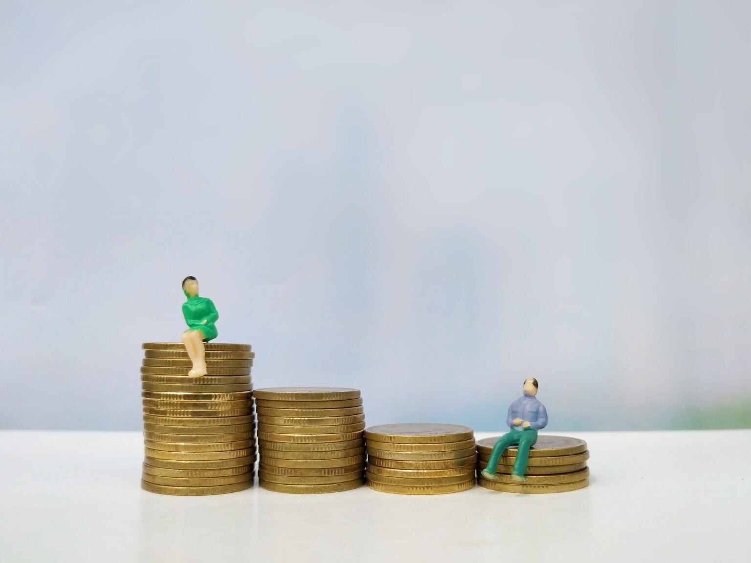 Eine Miniaturfigur bekam keine Gehaltserhöhung seit Jahren, sitzt auf wenig Geldstücken und schaut sehnsüchtig auf großen einen Geldhaufen.