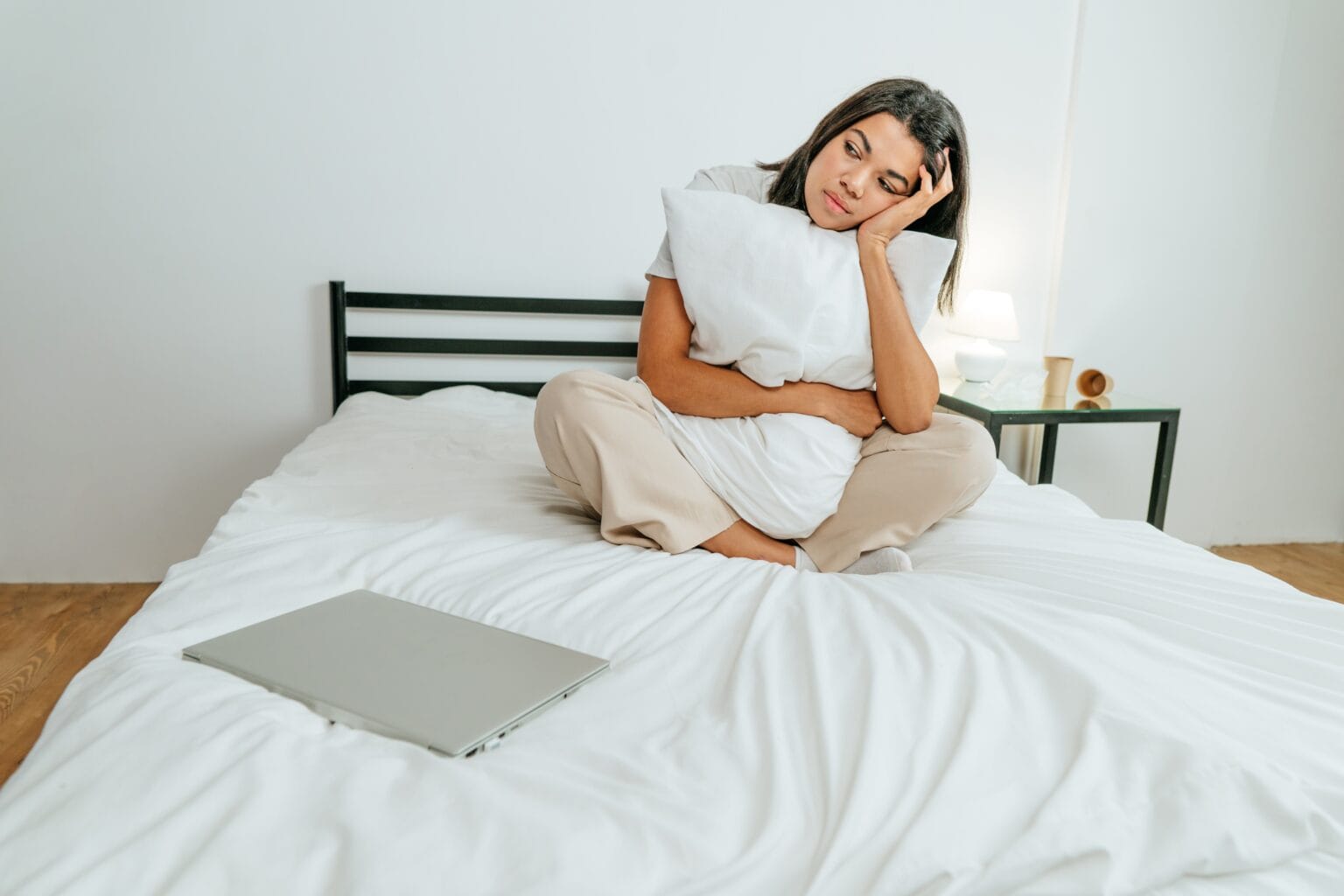 Eine junge Frau sitzt müde und unmotiviert auf dem Bett, vor ihr liegt ein zugeklappter Laptop.