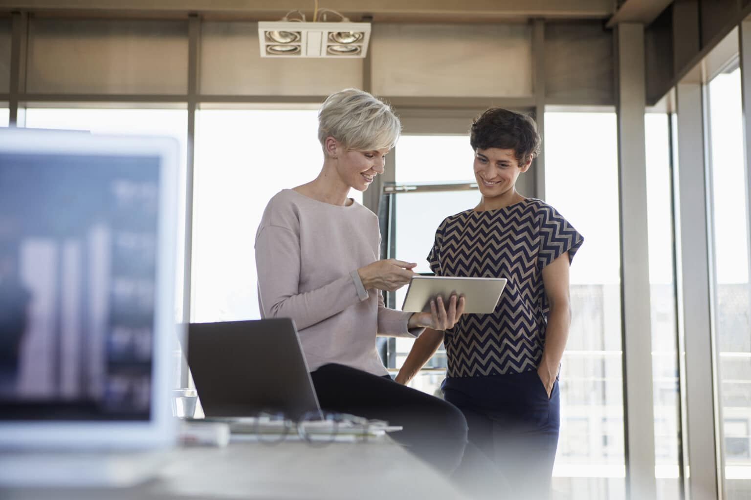 Zwei Geschäftsfrauen teilen sich Tablet im Büro und besprechen sich.