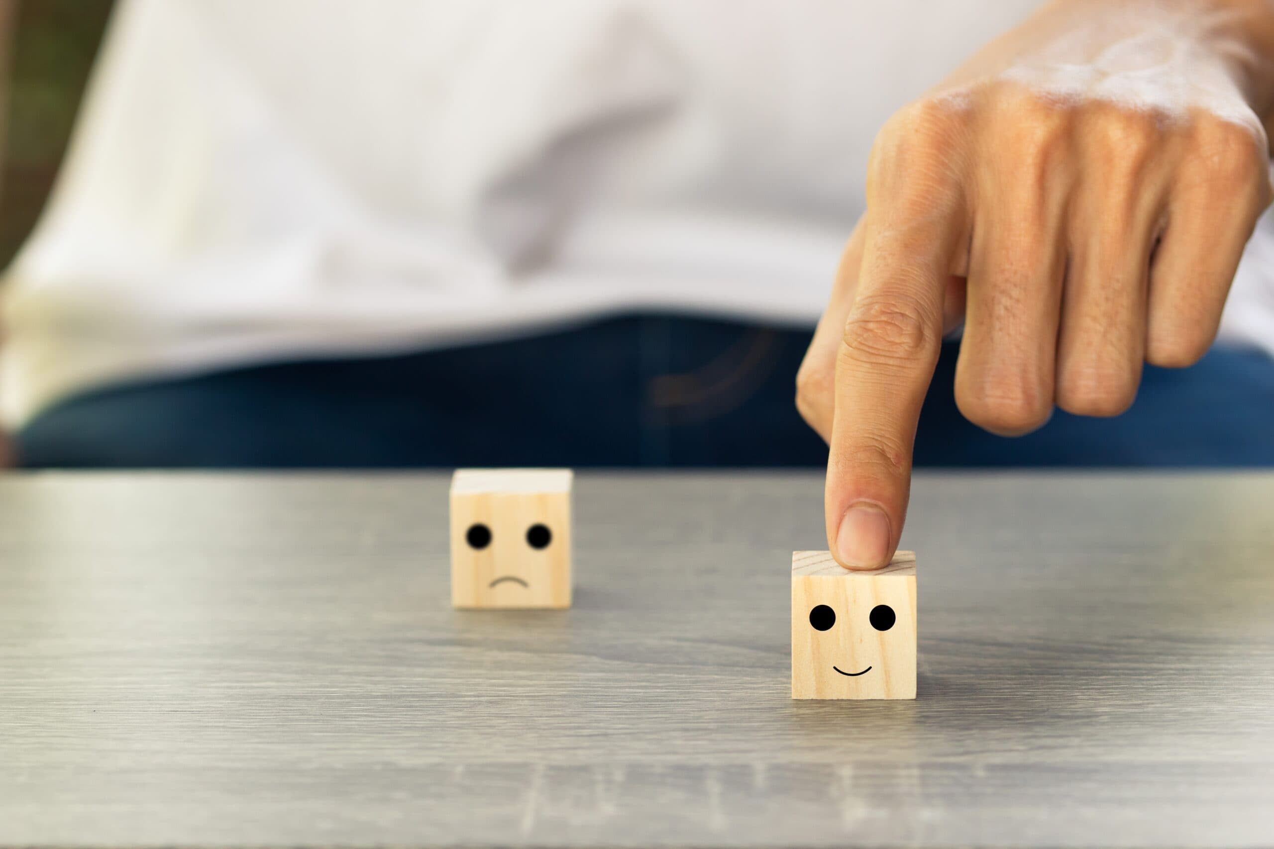 Eine Person kann aus zwei Holzwürfeln einen aussuchen, einen traurigen und einen lächelnden. Er wählt den lächelnden Würfel aus und schiebt diesen mit seinem Zeigefinger nach vorne.